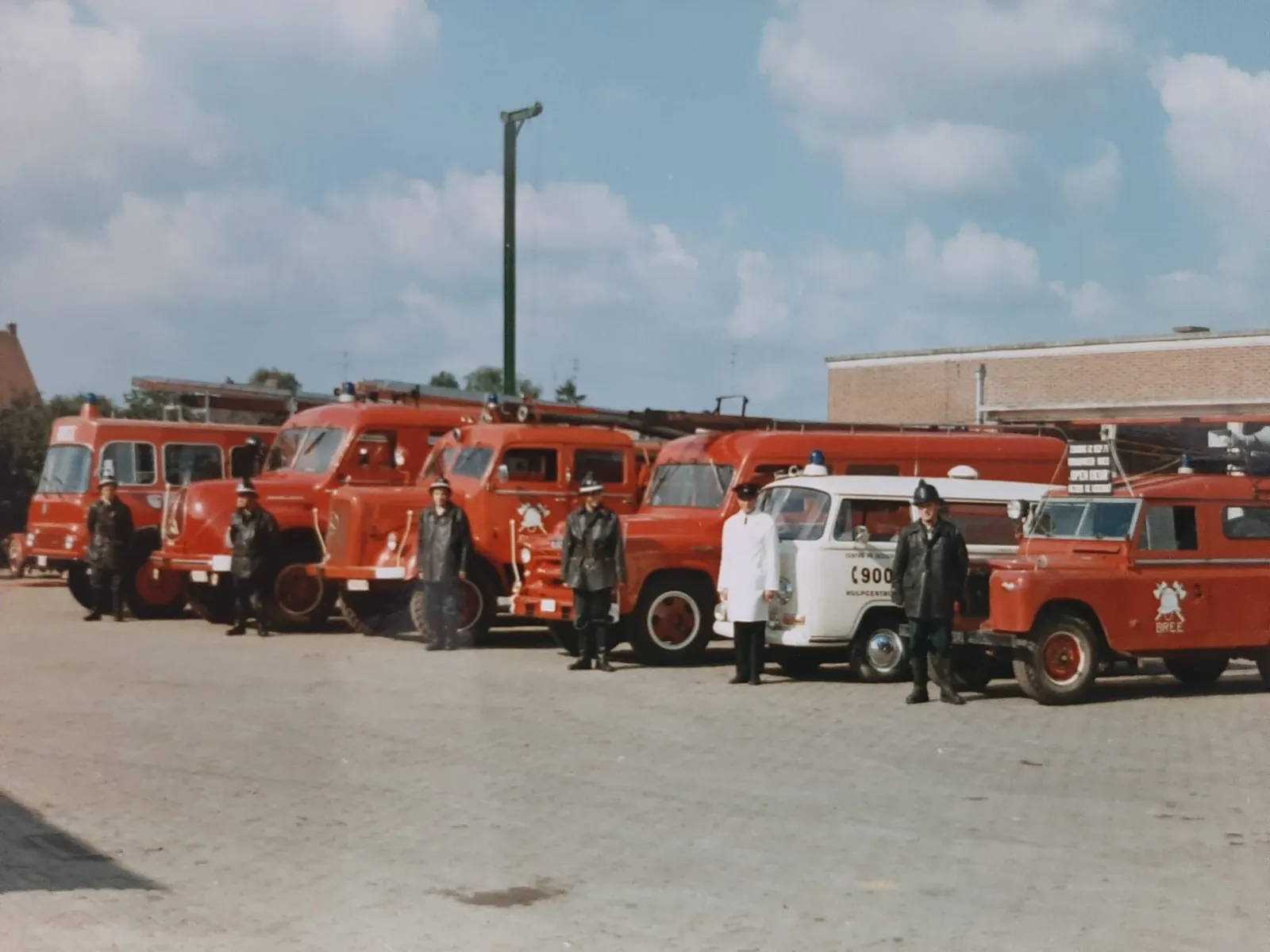 Rij historische brandweervoertuigen van Bree met brandweerlieden